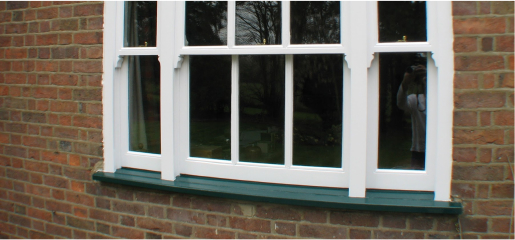 A white window with green trim undergoing a sash windows restoration project on a brick wall.