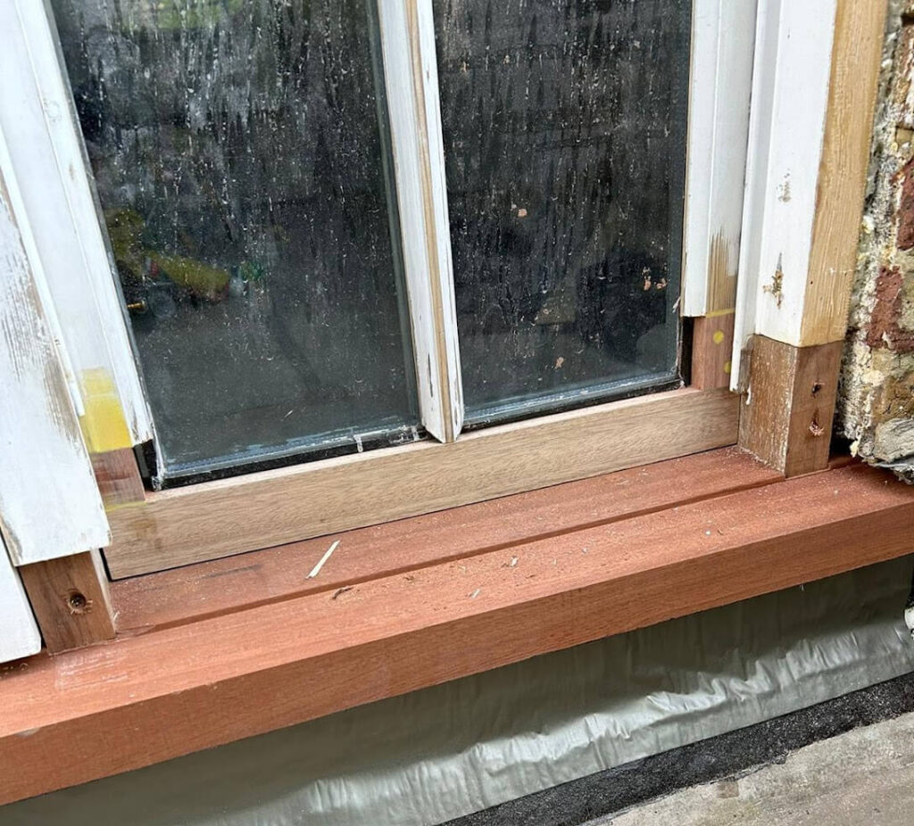 Close-up of a window sill showcasing chipped paint, dirt on the glass, and a recent wooden trim installation, reminiscent of the careful workmanship often seen in Sash Windows Repairs Croydon.