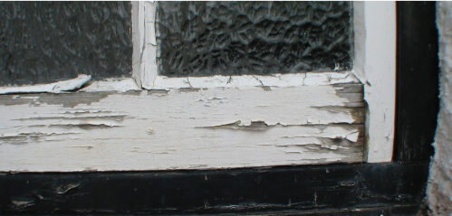 Close-up of a window frame with peeling white paint and textured glass panes, hinting at the need for window rot repair.