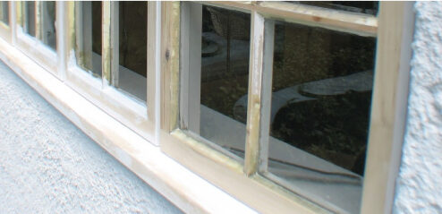 Close-up of a multi-paned wooden window with a reflective glass surface, showcasing expert window rot repair, set in a light-colored wall.