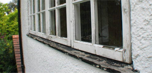 Close-up view of an old, weathered window with peeling paint on a white stucco wall, hinting at the need for window rot repair.